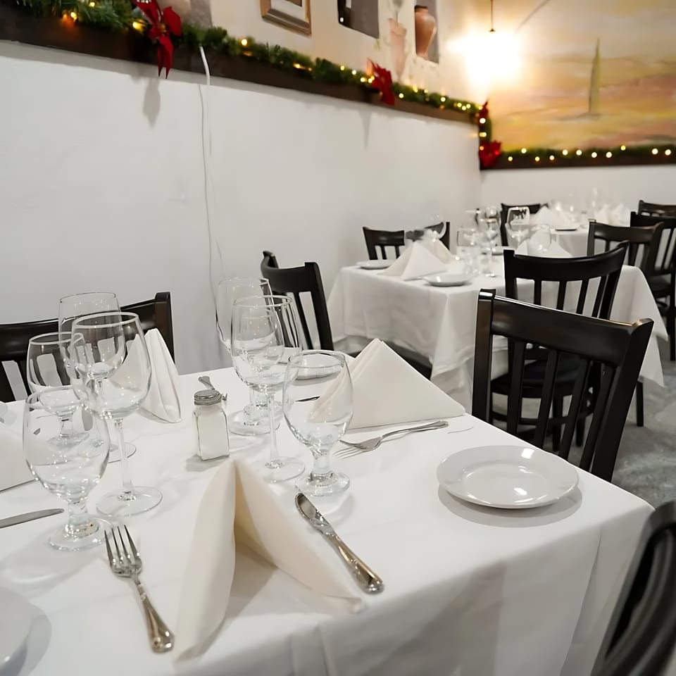 Set tables with white tablecloths, wine glasses, and dark chairs in Buona Sera Ristorante.