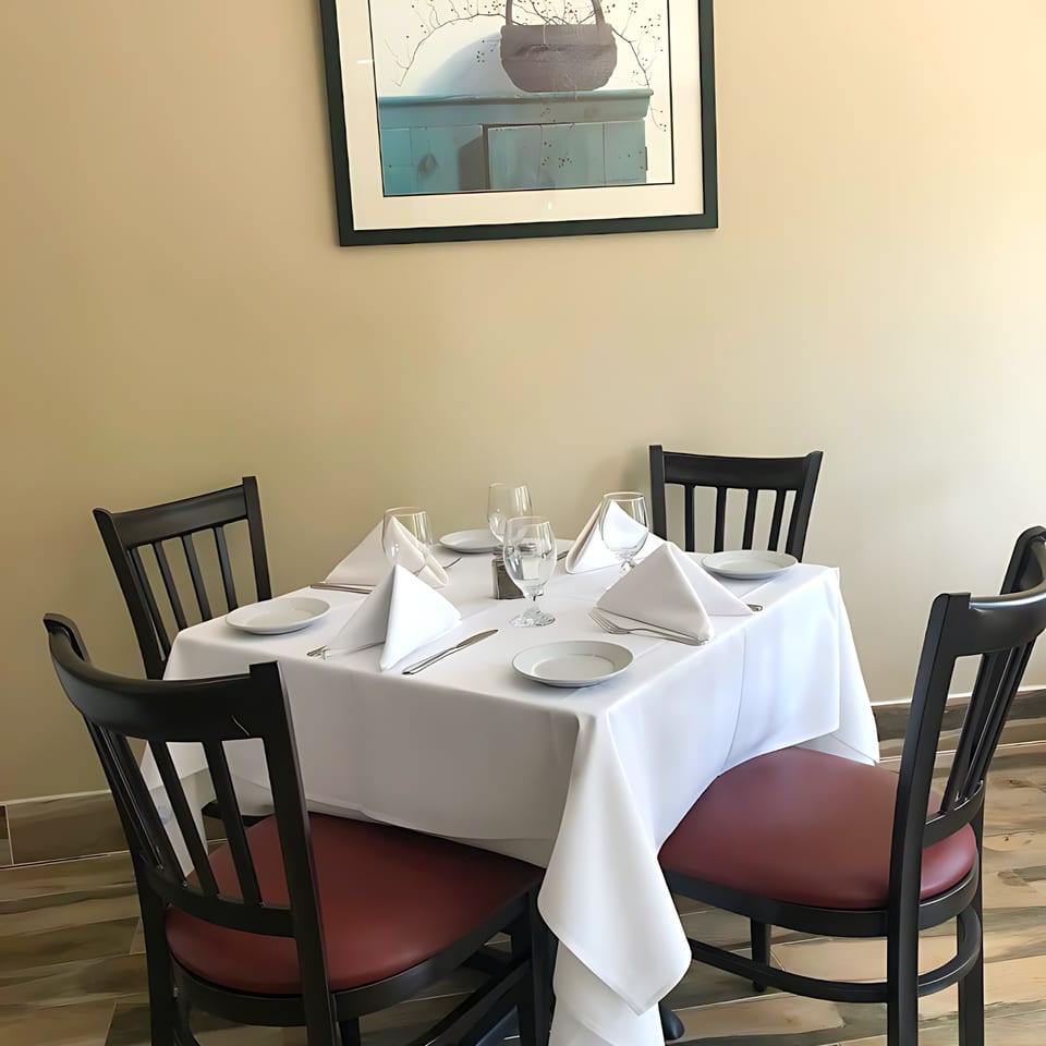 A set table for four with white tablecloths, napkins, and dark chairs with red seats at Buona Sera Ristorante.