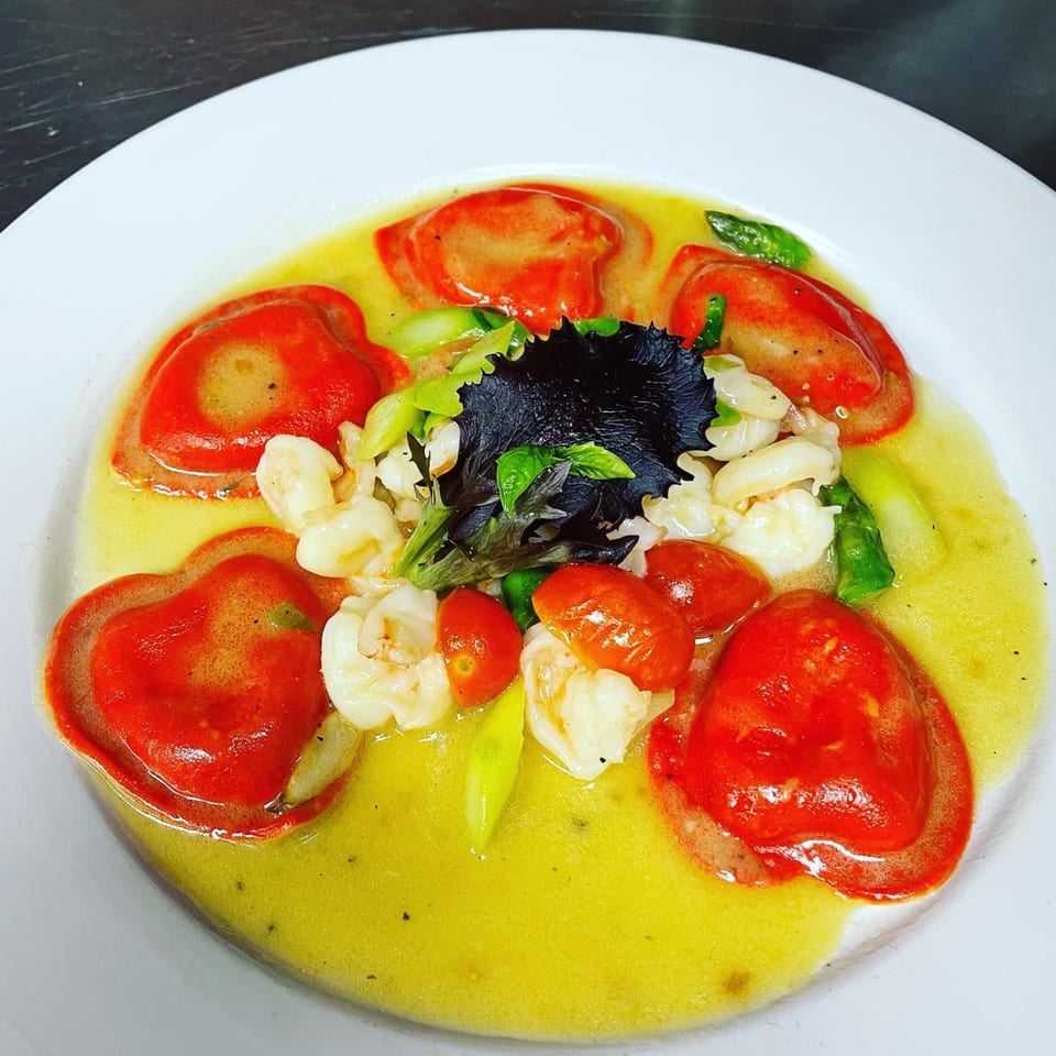Heart-shaped red ravioli in a yellow sauce with shrimp, cherry tomatoes, and greens.