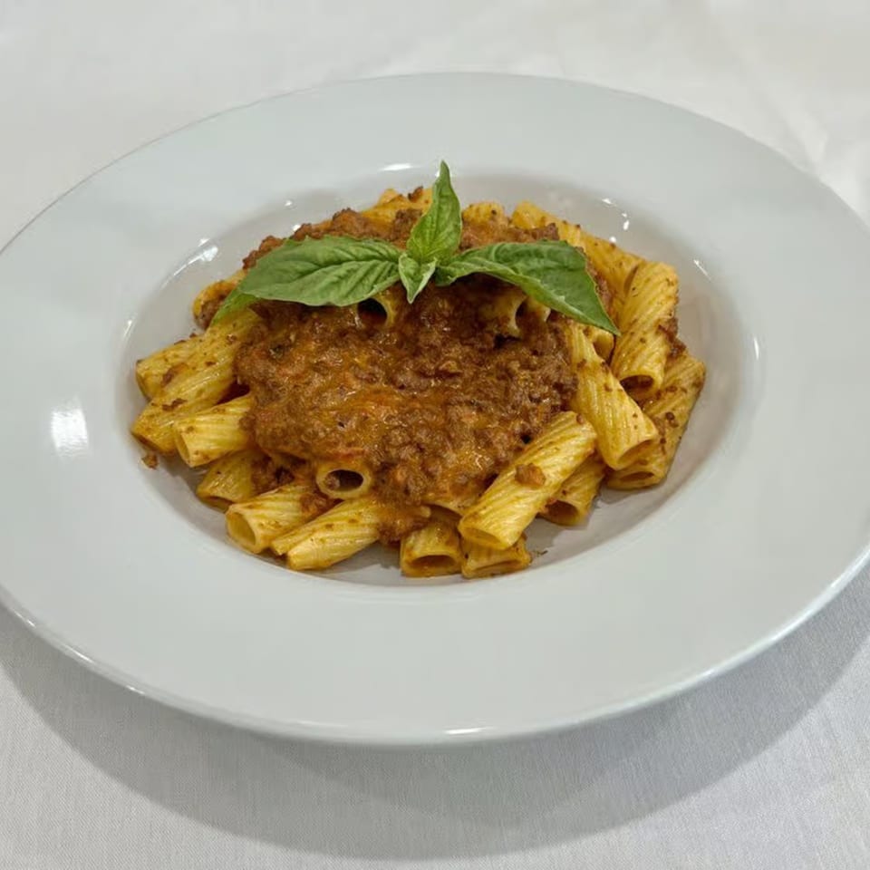 Rigatoni pasta with a rich Bolognese sauce and fresh basil on a white plate.