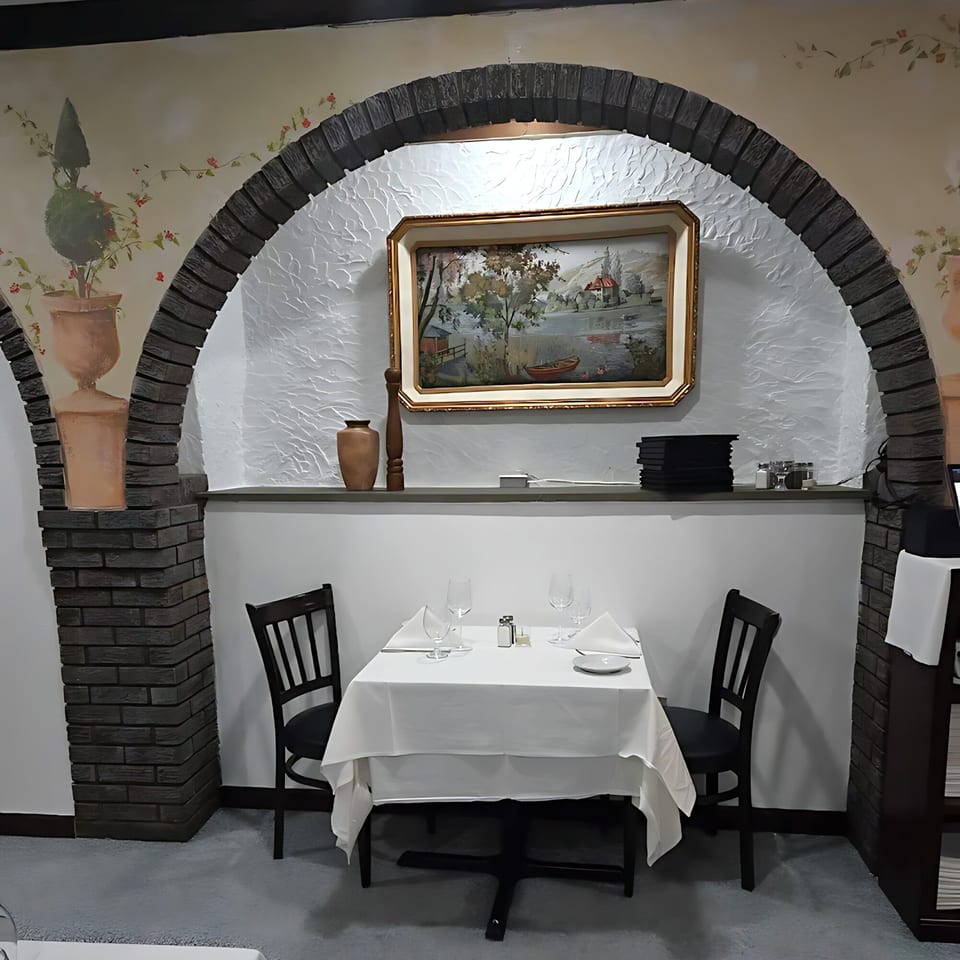 An Italian restaurant interior with a set table for two under a brick archway and painting.