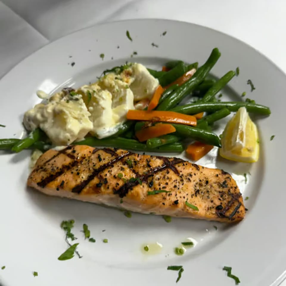 Grilled salmon with green beans, carrots, mashed potatoes, and a lemon wedge on a white plate.